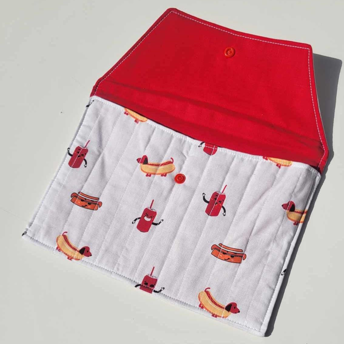 Handmade, lightly quilted tablet or document holder with a snap closure. Exterior fabric is a playful Dachshund hot dog and cola pattern with a bright red interior fabric.