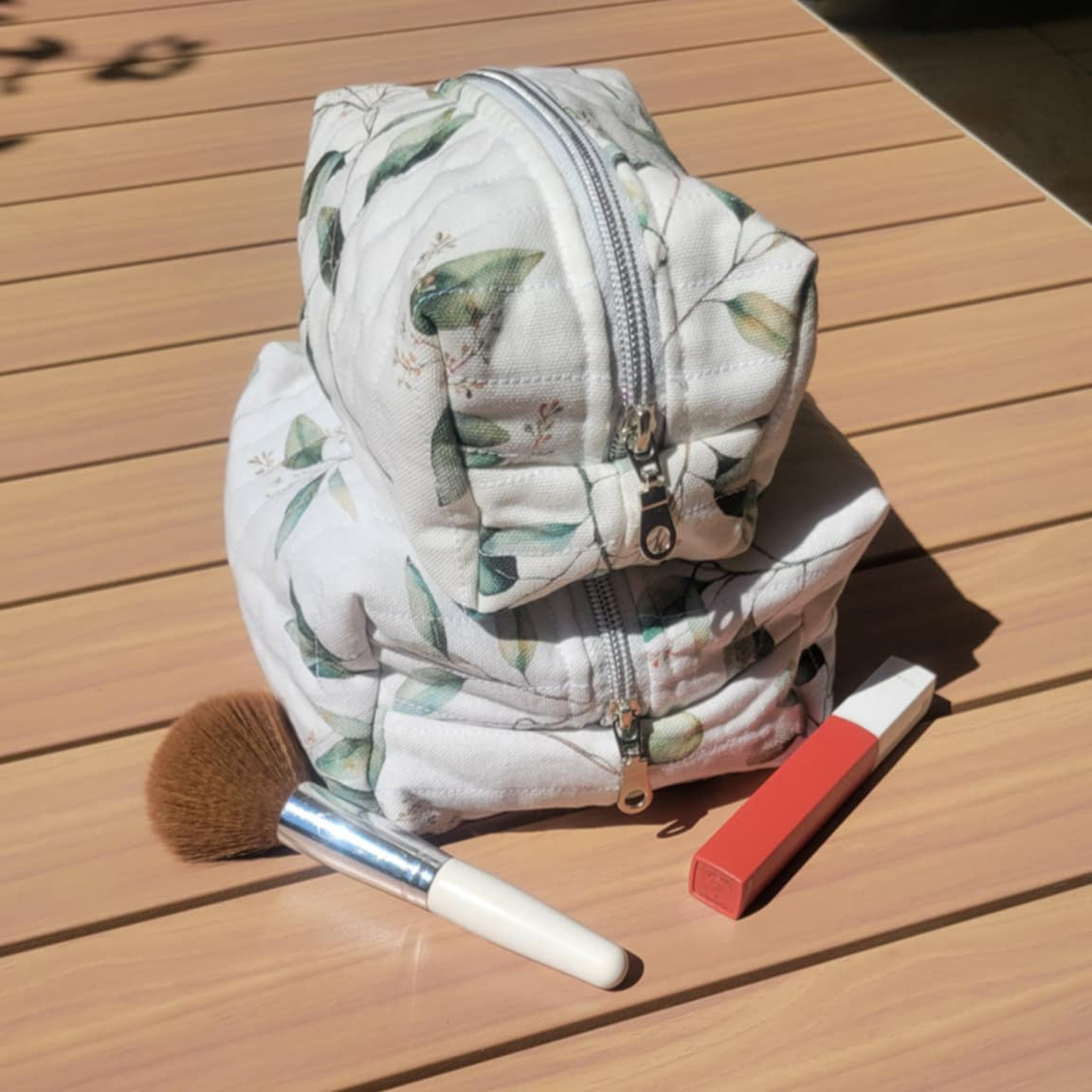Small floral-patterned makeup bag on a wooden surface with makeup items around