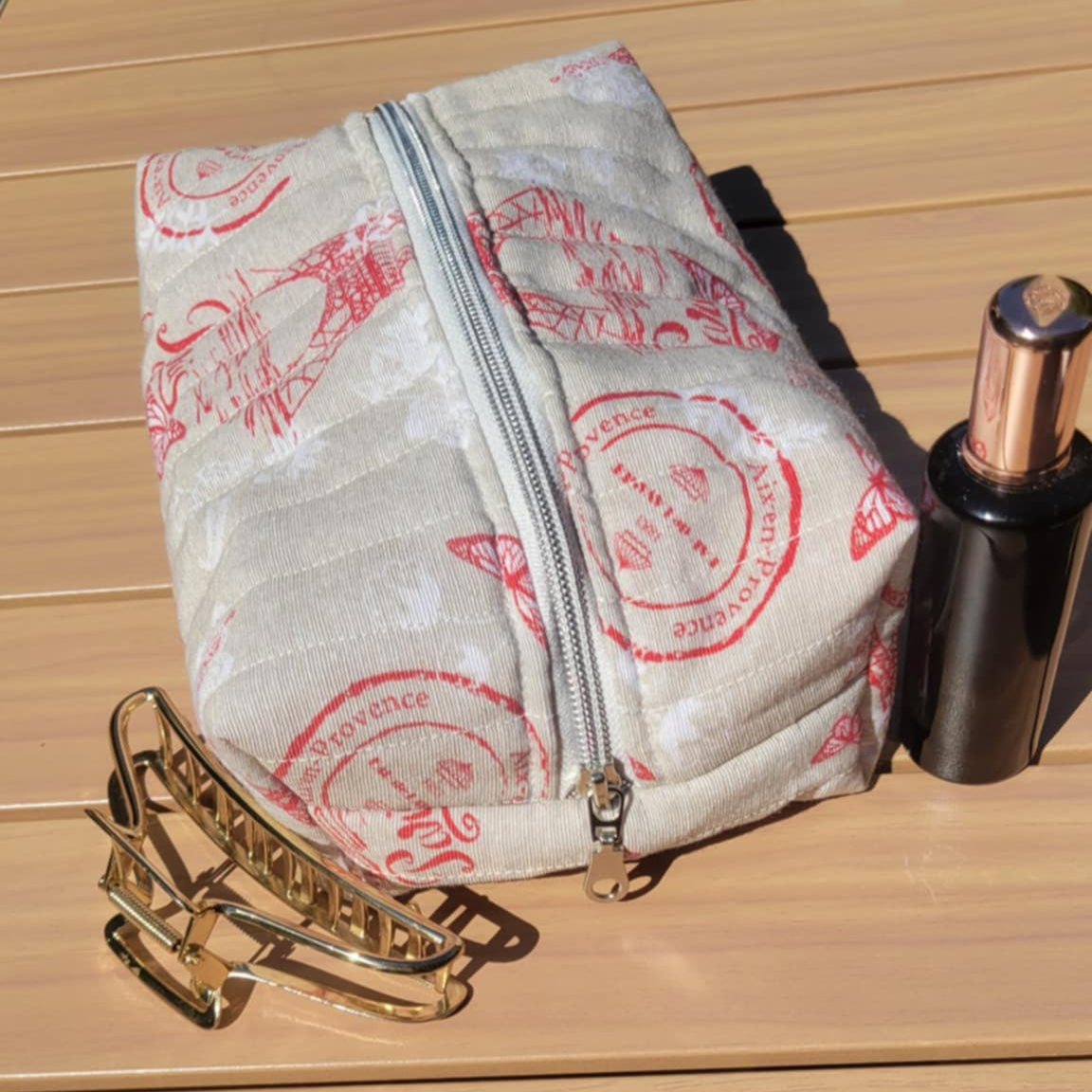 Makeup bag with pink designs on a wooden surface with makeup items around