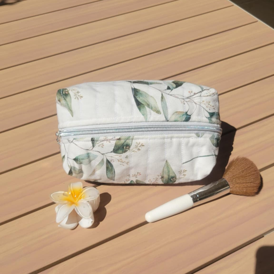 Cosmetic bag with floral pattern, flower, and makeup brush on a wooden surface