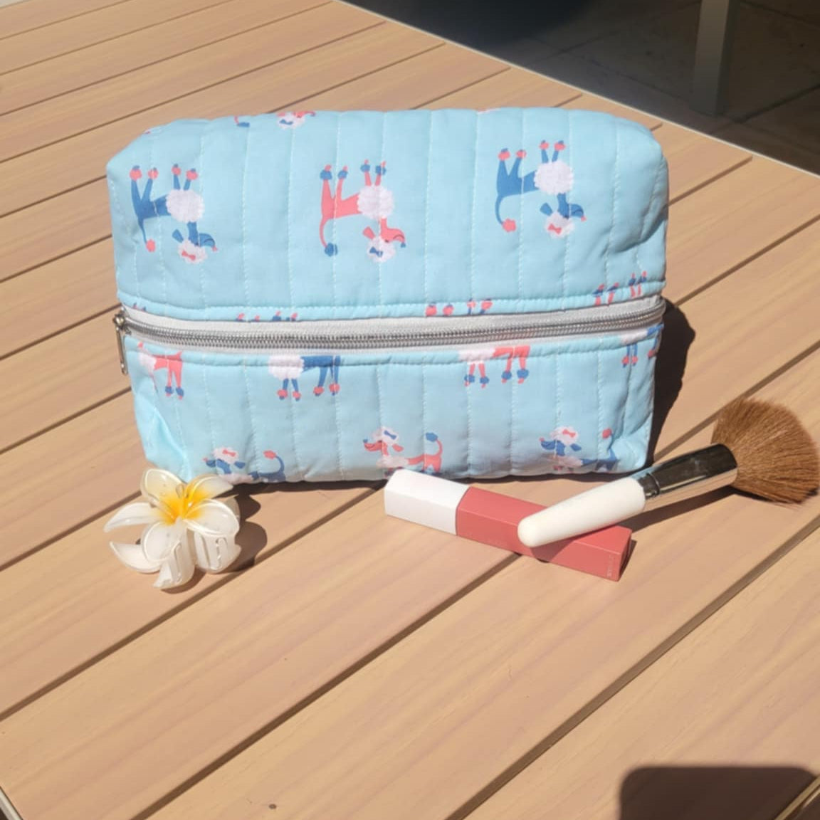 Blue cosmetic bag with horse pattern on a wooden surface with a flower and brush.