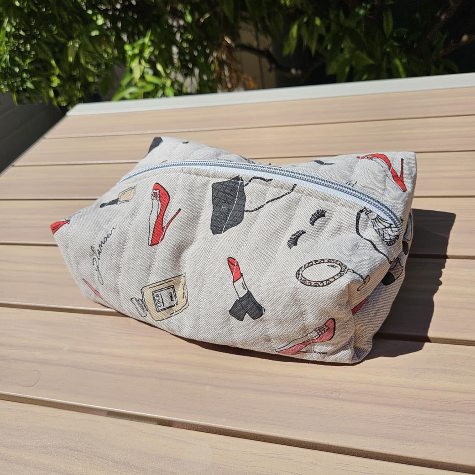 Fabric pouch with makeup illustrations on a wooden surface