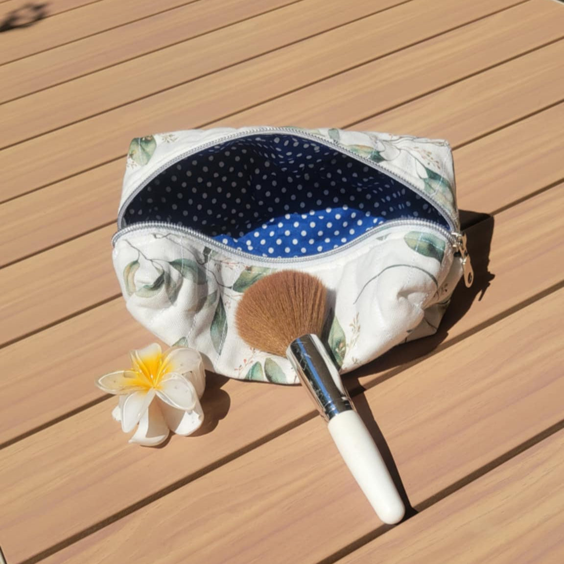 Makeup bag with a brush and flower on a wooden surface