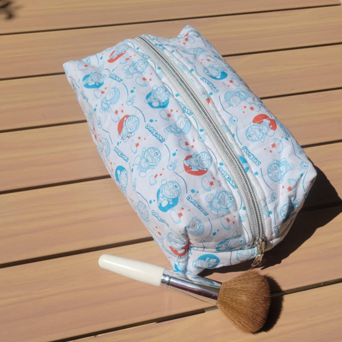 Cosmetic bag with a pattern on a wooden surface, accompanied by a brush.