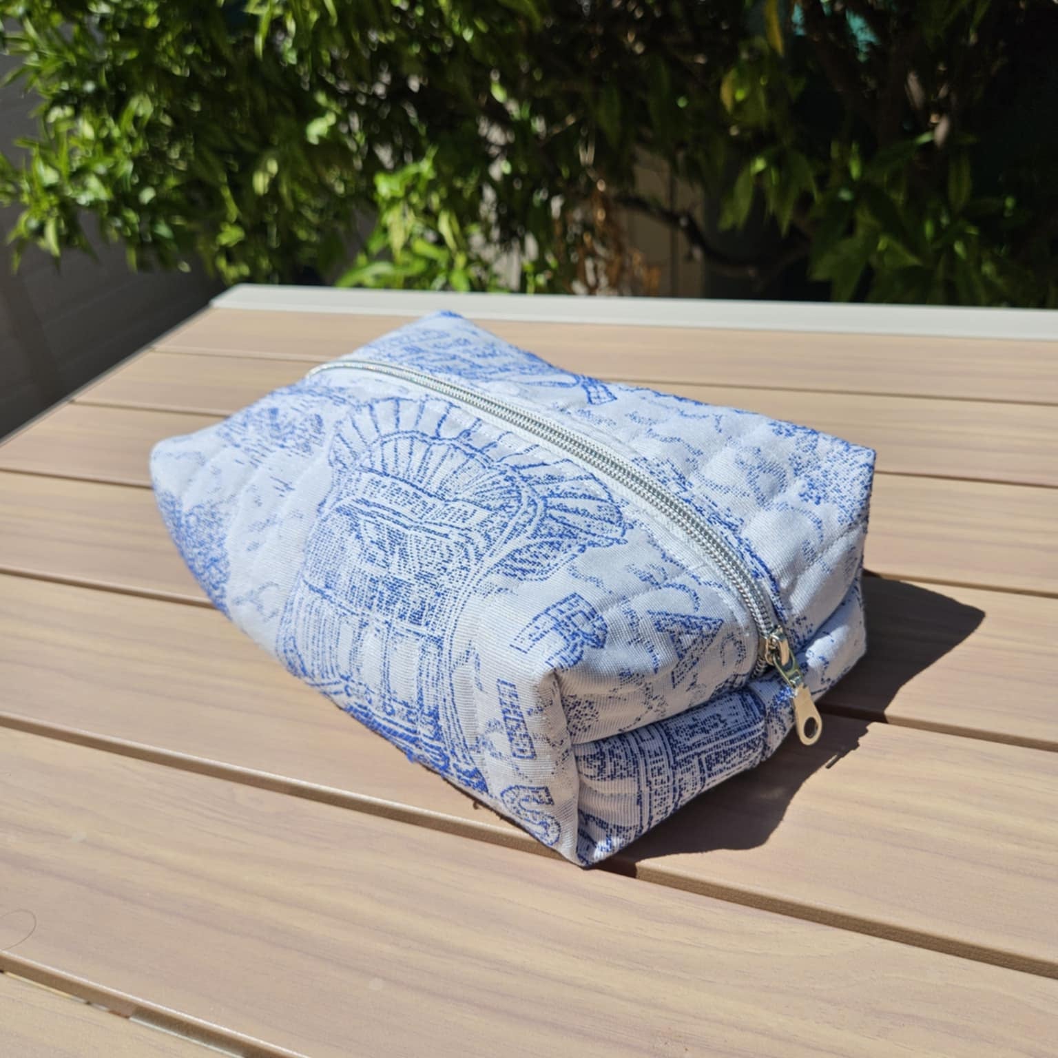Blue and white patterned pouch on a wooden surface with greenery in the background