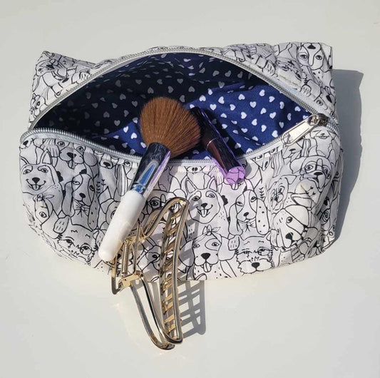 Handmade, lightly quilted storage pouch made with a whimsical black and white dog fabric with a silver zipper closure. There is a navy blue and white hearts cotton fabric for the interior.
