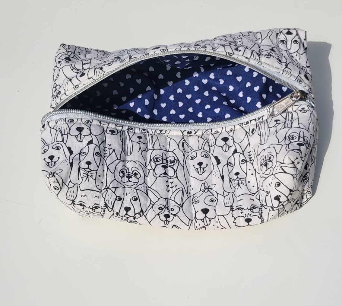 Handmade, lightly quilted storage pouch made with a whimsical black and white dog fabric with a silver zipper closure. There is a navy blue and white hearts cotton fabric for the interior.