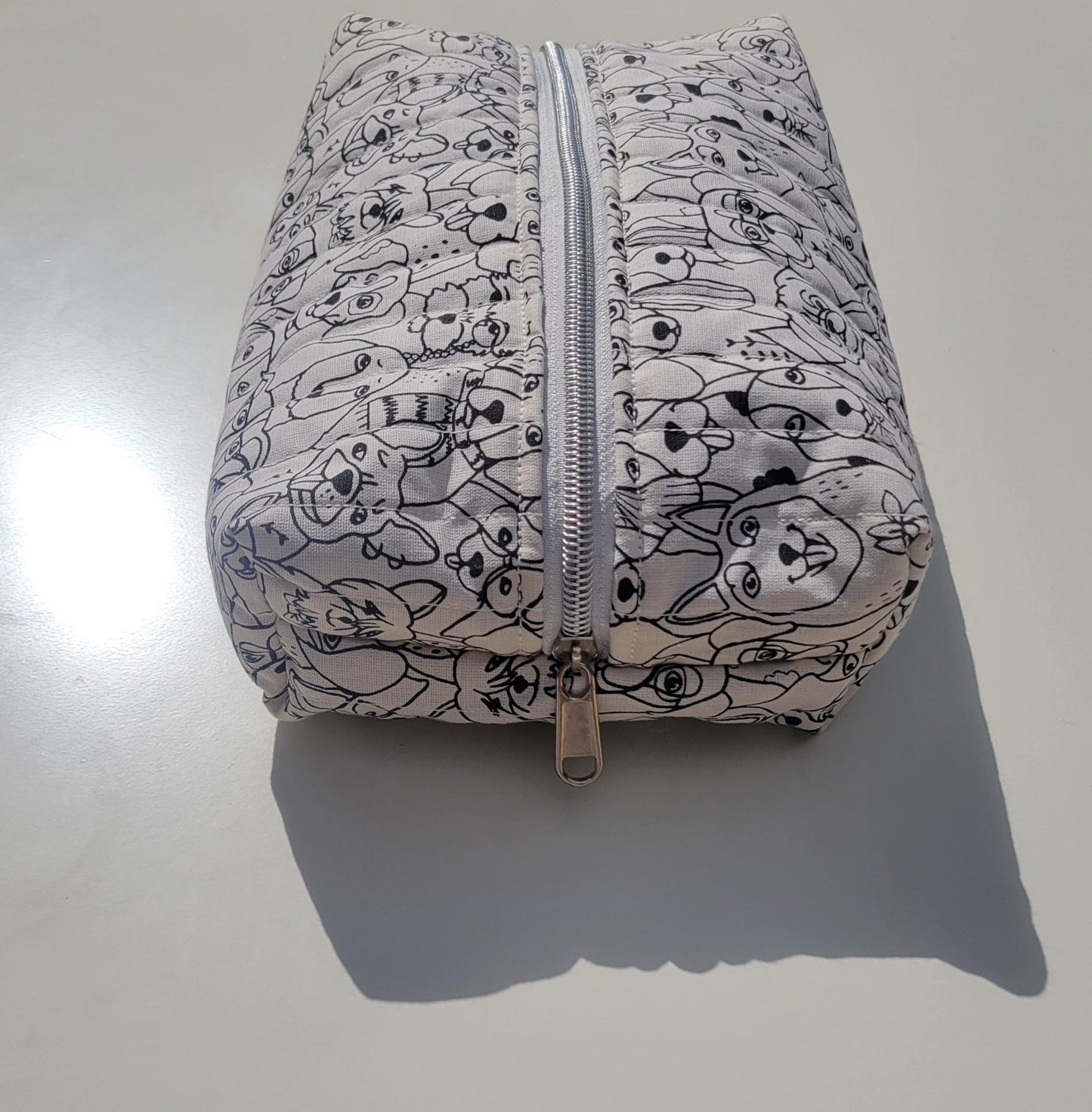 Handmade, lightly quilted storage pouch made with a whimsical black and white dog fabric with a silver zipper closure.