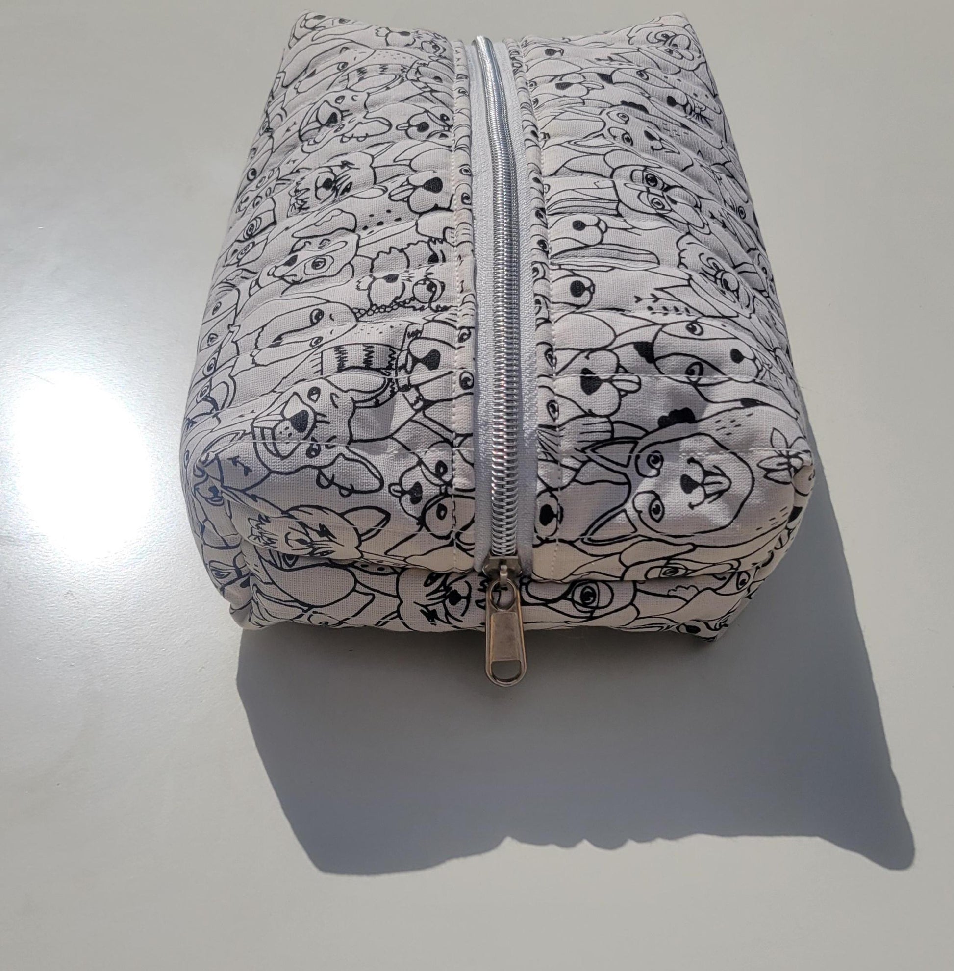 Handmade, lightly quilted storage pouch made with a whimsical black and white dog fabric with a silver zipper closure.