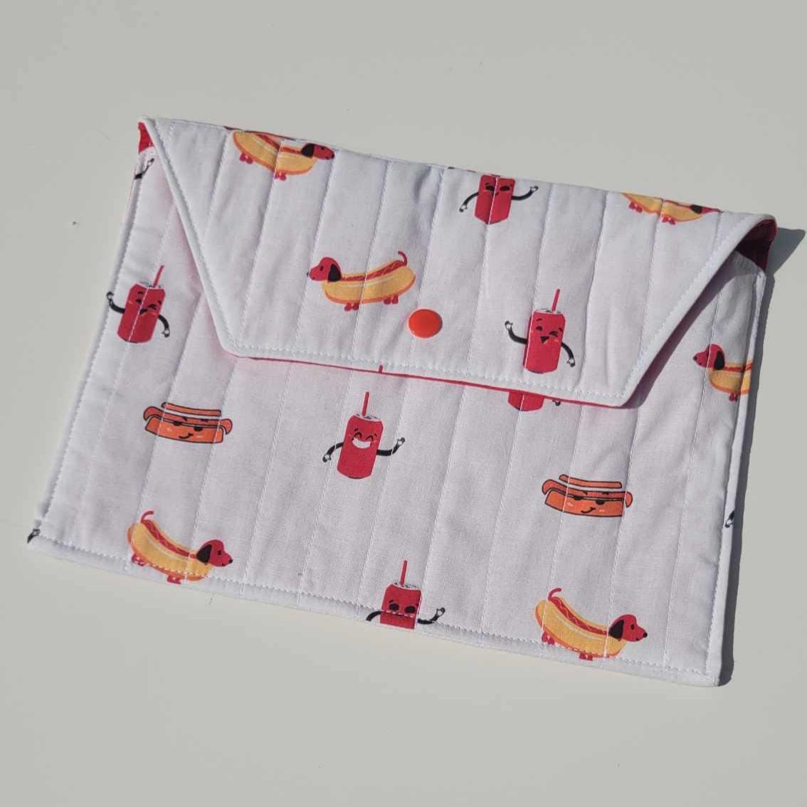 Handmade, lightly quilted tablet or document holder with a snap closure. Exterior fabric is a playful Dachshund hot dog and cola pattern with a bright red interior fabric.