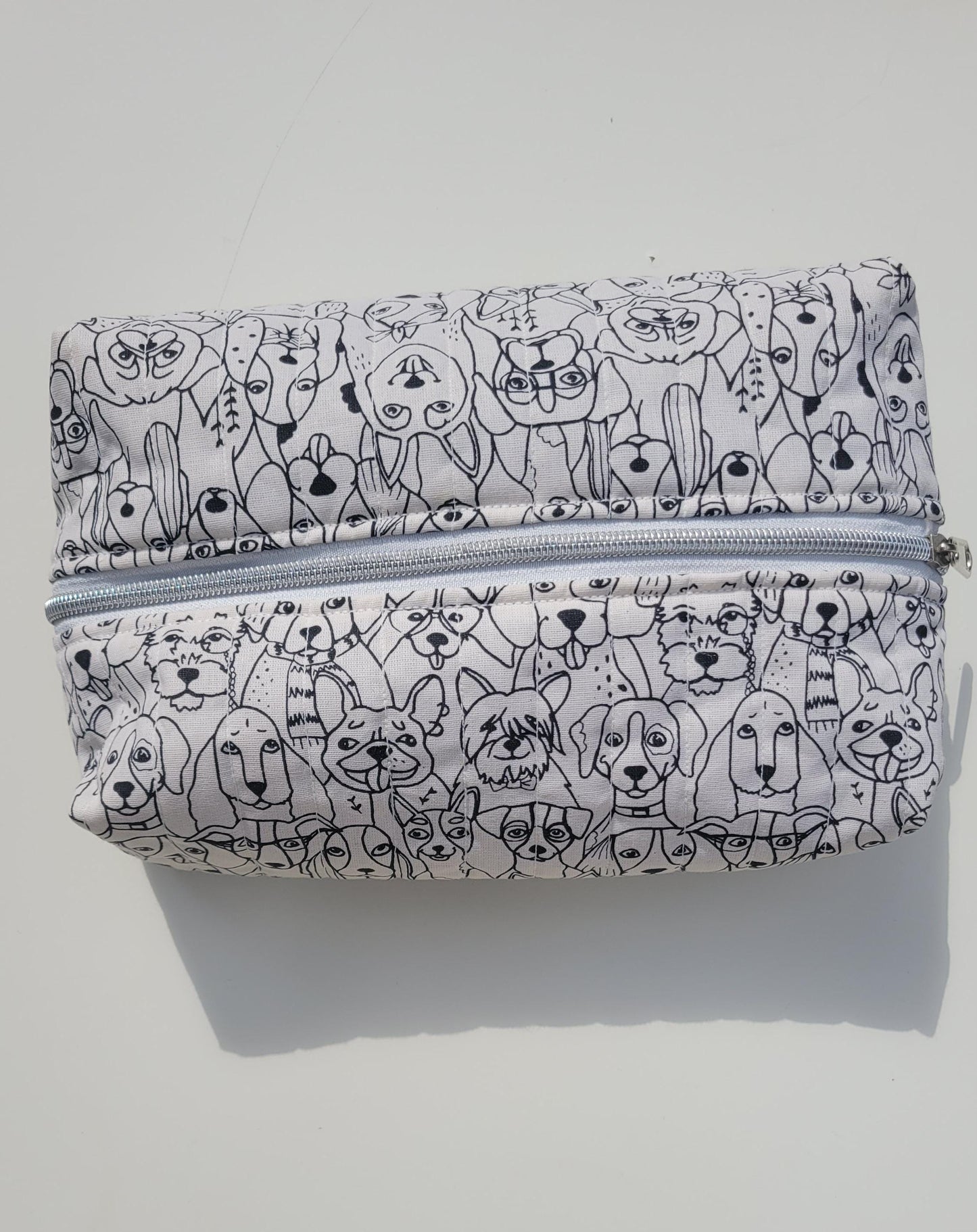 Handmade, lightly quilted storage pouch made with a whimsical black and white dog fabric with a silver zipper closure.