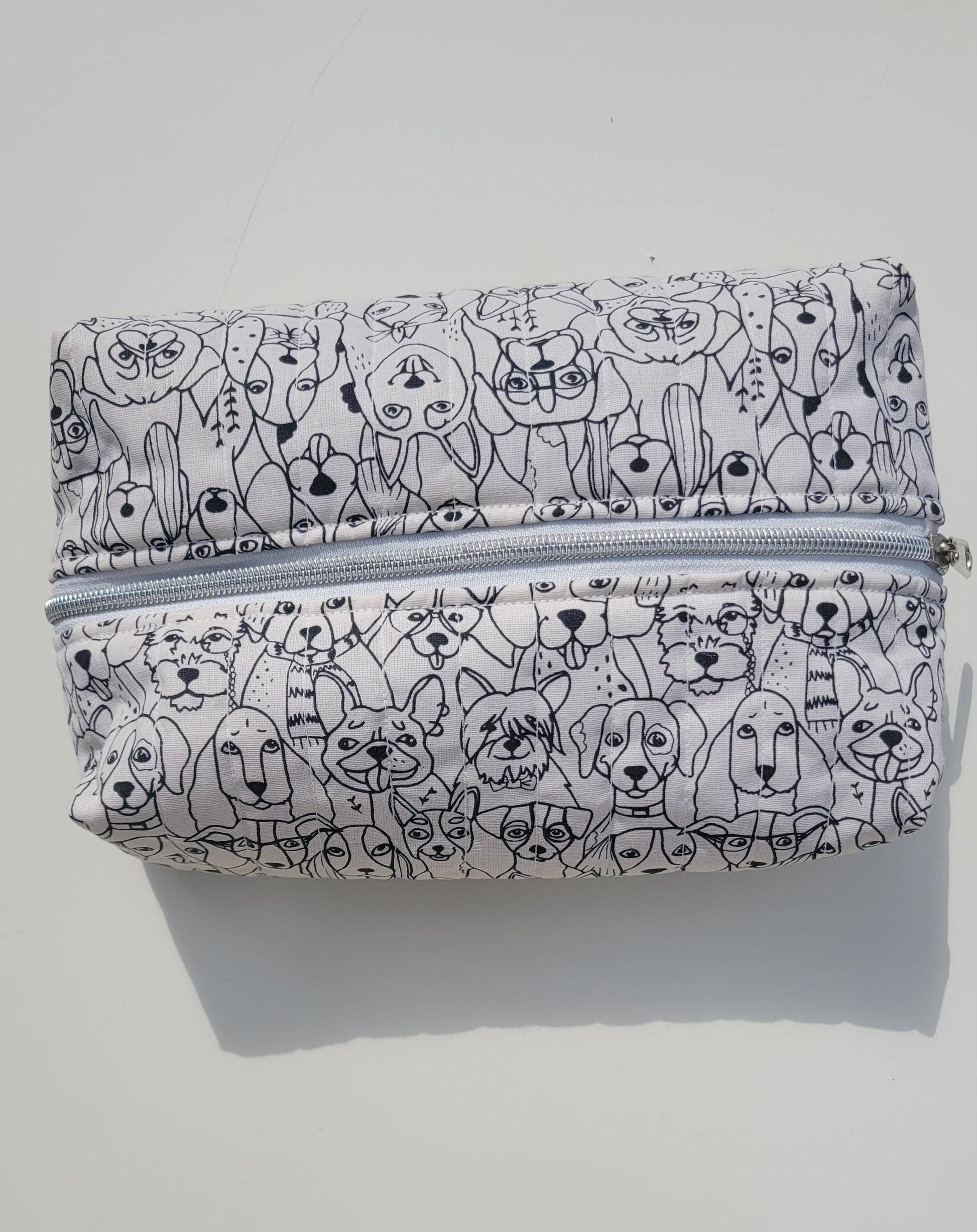 Handmade, lightly quilted storage pouch made with a whimsical black and white dog fabric with a silver zipper closure.