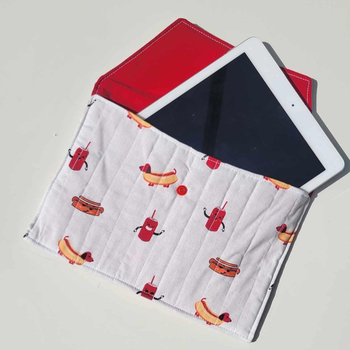 Handmade, lightly quilted tablet or document holder with a snap closure. Exterior fabric is a playful Dachshund hot dog and cola pattern with a bright red interior fabric.