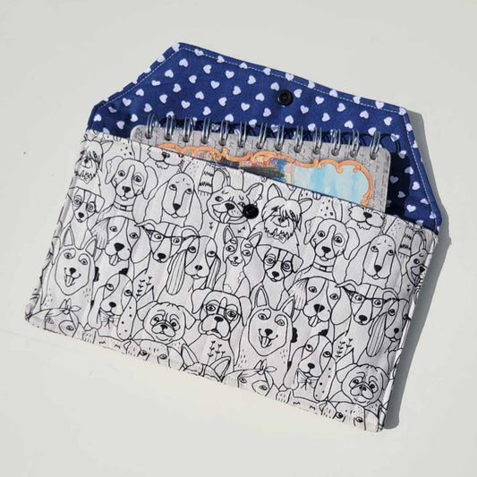 Handmade e-reader or document holder with a black and white dog print for the exterior fabric and a navy blue and white heart fabric for the interior. It is lightly quilted with a snap closure.