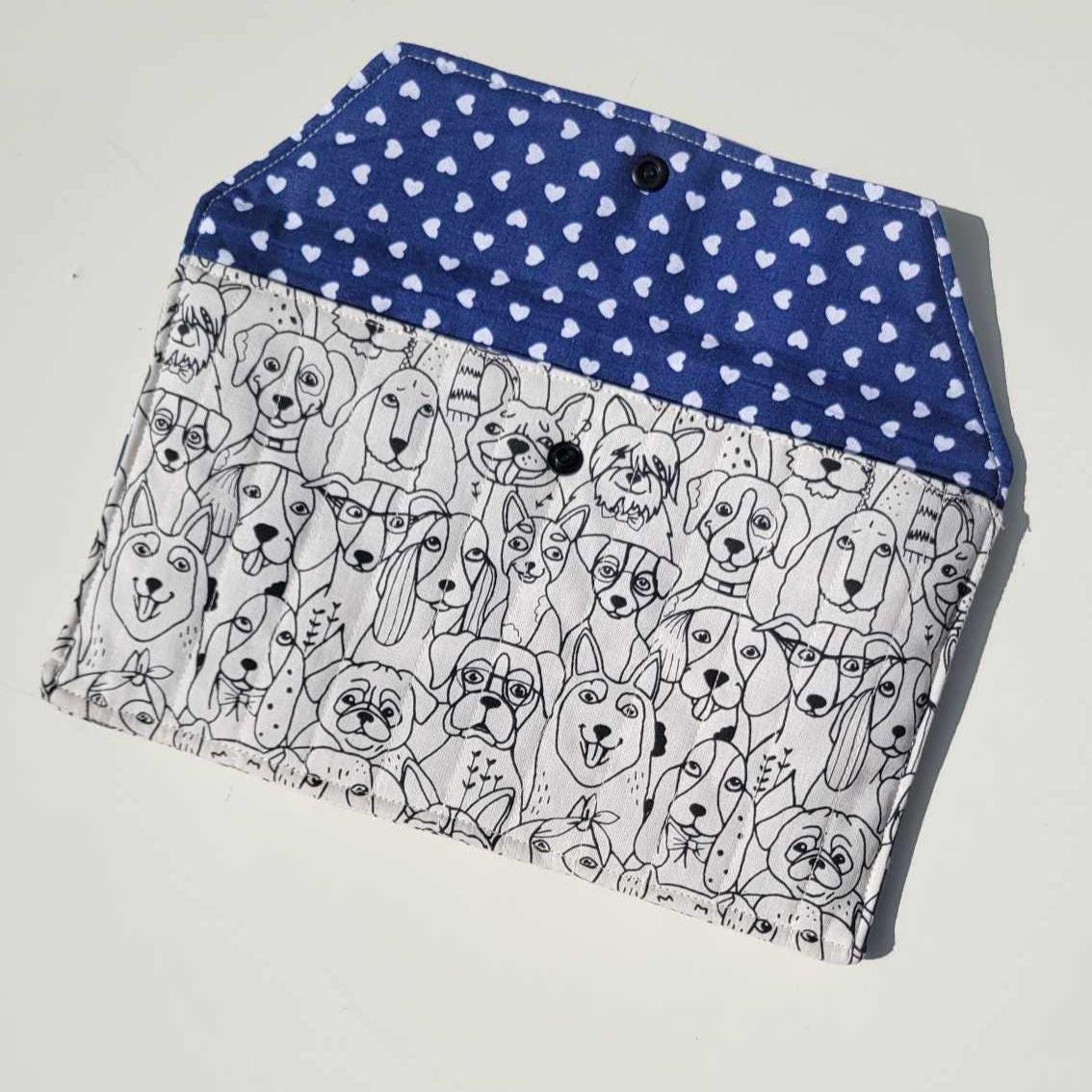 Handmade e-reader or document holder with a black and white dog print for the exterior fabric and a navy blue and white heart fabric for the interior. It is lightly quilted with a snap closure.